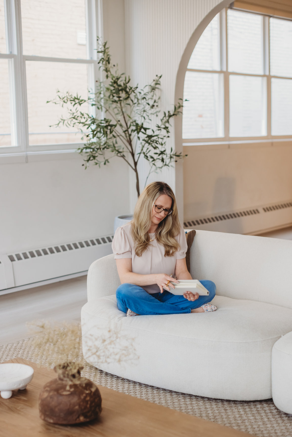 Sarah Hope sitting on a cream sofa in soft window light, journaling quietly